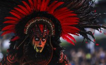 A performer wears heavy makeup, colored contacts, and a large feathery costume during a parade.