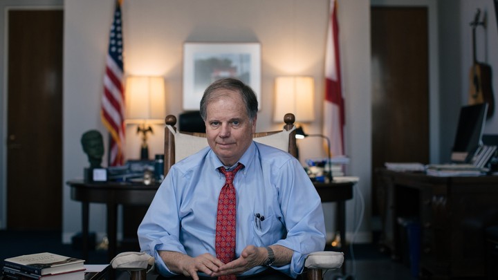 Framed by the U.S. and Alabama state flags, Doug Jones sits in an office.