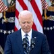 a photo of Joe Biden at a microphone, U.S. flags behind him, with his eyes closed