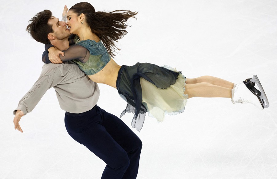 A figure skater clings closely to her partner as he appears to spin her in the air.