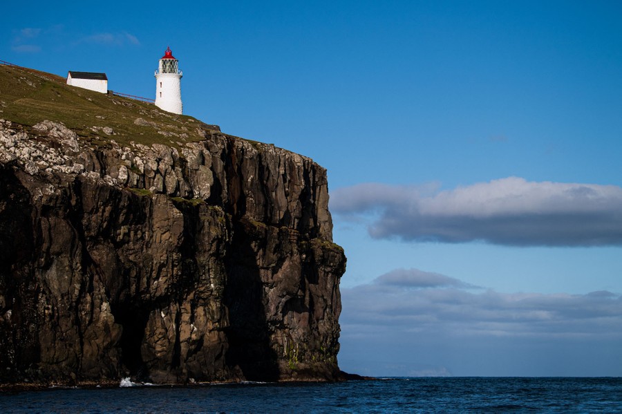 A lighthouse stands high on a sea cliff.