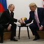 Trump and Putin, seated, shake hands.