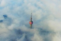 The spire of a skyscraper rising above a a bed of clouds