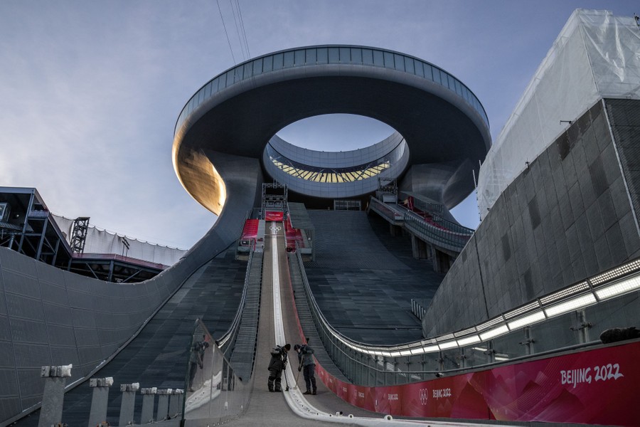 Two workers sweep the bottom of a slope at a large ski jump facility.