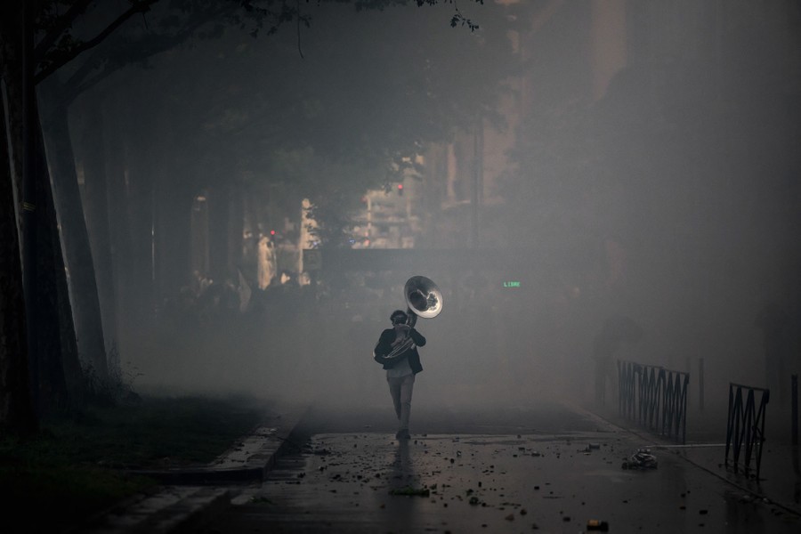 A protester plays a sousaphone, walking on a deserted road, through a cloud of tear gas.