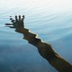 A hand reflected in ripples across blue water