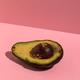 An avocado on a millennial pink background.