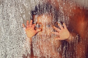 The blurry outline of a parent holding a child with their hands pressed to a glass pane covered in water droplets