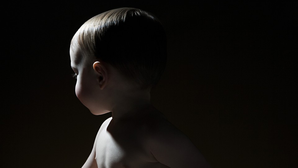 A shirtless baby turns away in a black background.