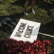 A photo of the legs of a person standing on a patch of grass next to a placard on the ground that reads "Vaccine Choice"