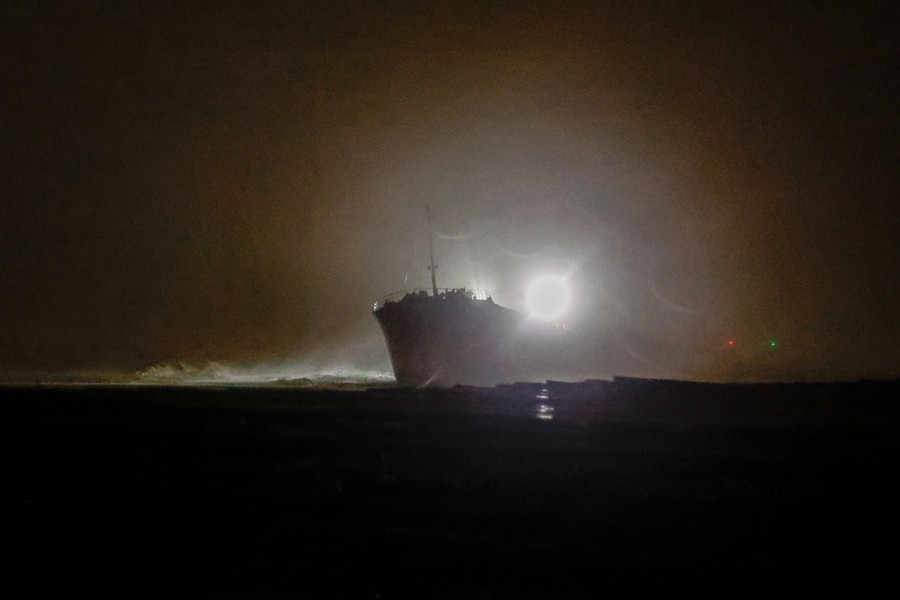 A night view of a stranded cargo ship in silhouette during a storm