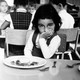 a child sitting with he hand on her mouth in front of a plate of food
