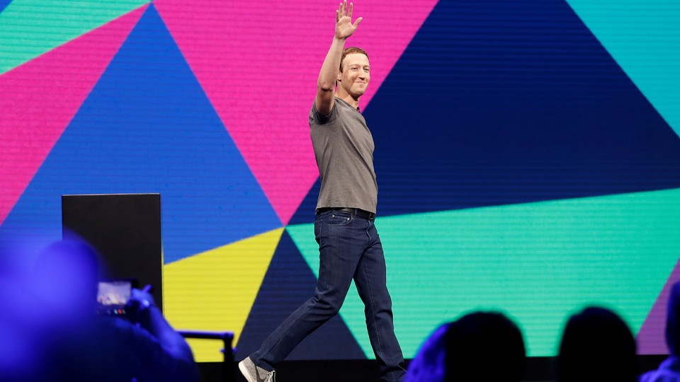 Mark Zuckerberg raises his hand while walking across a stage.