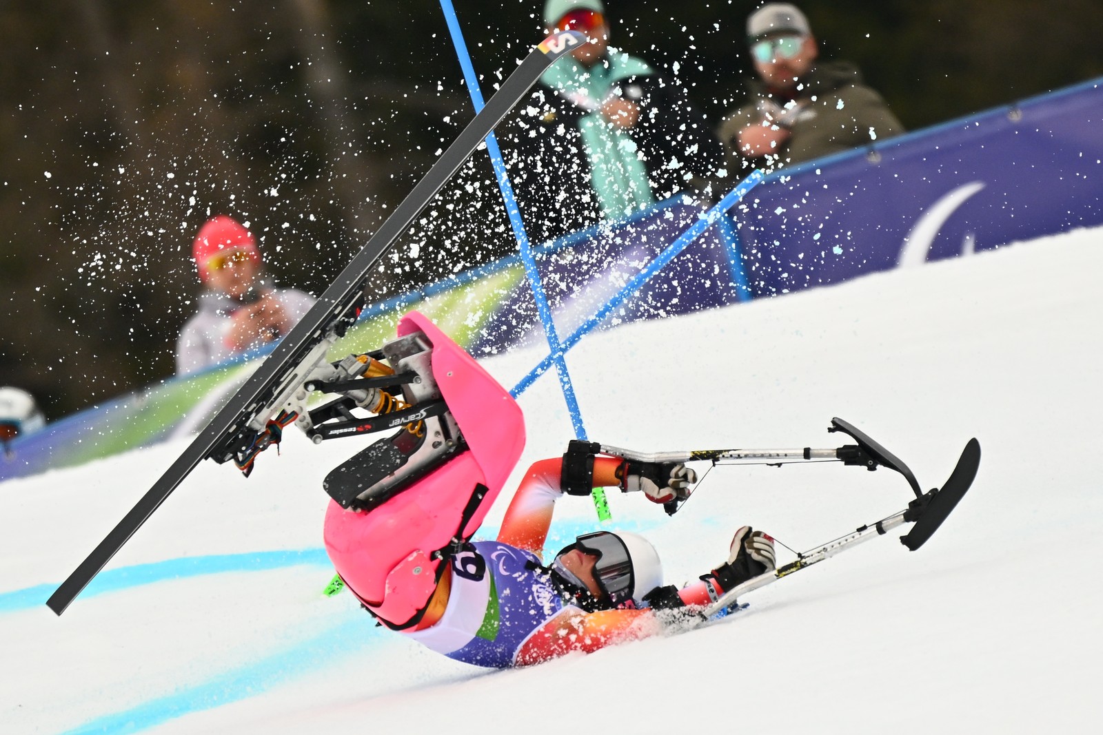 A seated para-alpine skier on a fast run crashes and tumbles on a ski slope.