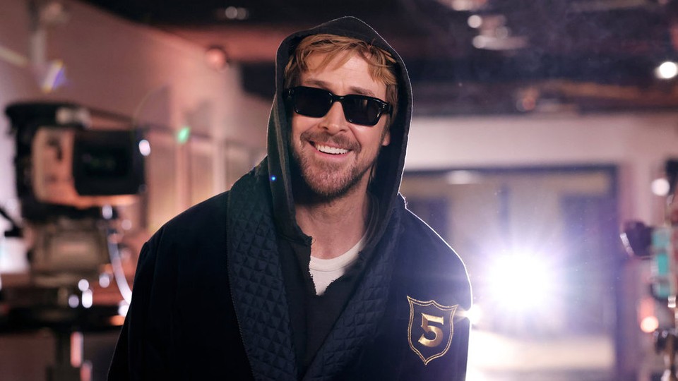 The actor Ryan Gosling smiles, wearing black sunglasses and a hood over his head