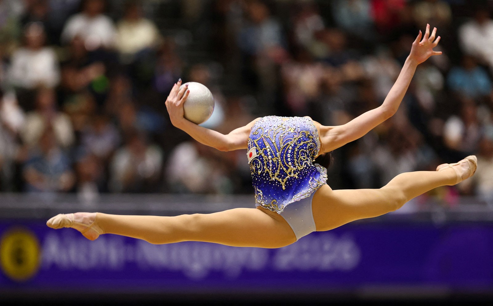 A gymnast leaps high in the air, their head tilted so far back. It appears to be missing.