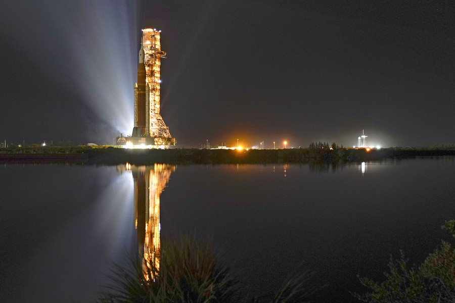 A tall rocket is transported to a launch pad at night.