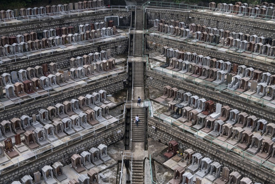 People walk on stairs among gravesites on a tiered hillside cemetery.