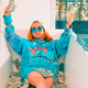 A young girl wearing a blue hoodie and blue sunglasses sitting in a bathtub full of dollar bills