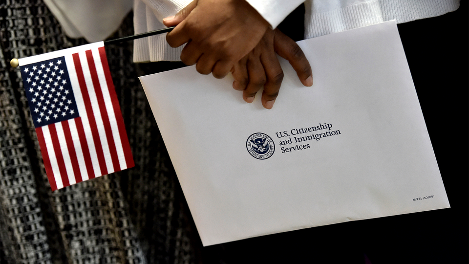 Photograph of hands holding a U.S. flag and an envelope labeled “U.S. Citizenship and Immigration Services”