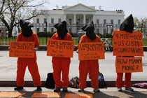 Four activists dressed up as Guantanamo Bay prisoners in front of the White House hold signs that accuse the U.S. administration of ignoring the deaths of prisoners waiting to be released from the U.S. prison in Cuba.