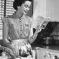 A woman reads a cookbook next to a mixer.