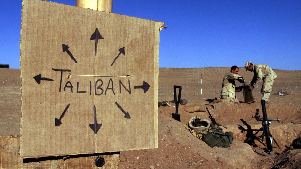 Two Marines fill a sandbag near a sign that says "Taliban"