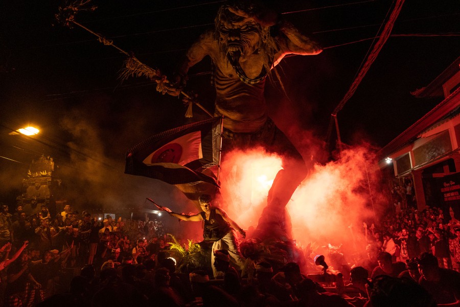 A crowd gathers beneath a large demonic sculpture.