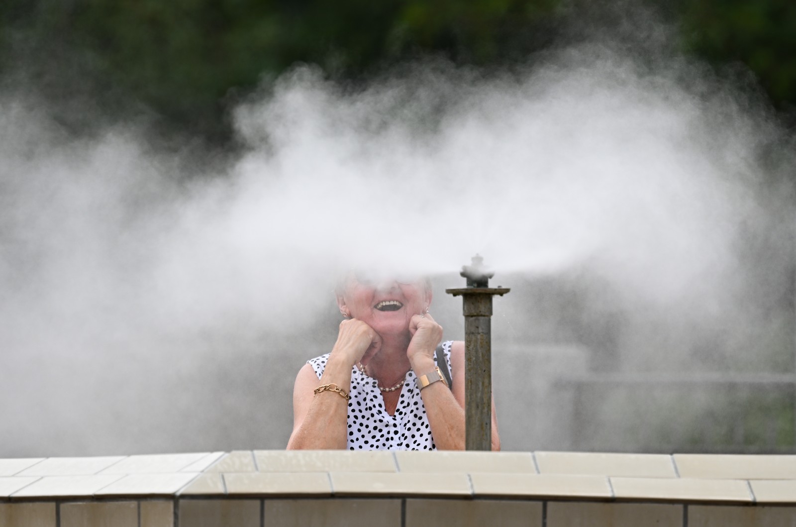 A woman smiles while breathing in mist from a nearby fountain.