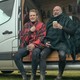 Two men in kilts sit in the open door of a van