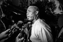A black-and-white photo of Eric Adams being questioned by the press.