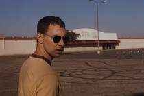 Jack Antonoff in a yellow shirt and sunglasses standing in a parking lot
