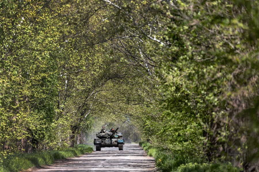 A tank rolls down a tree-lined street.