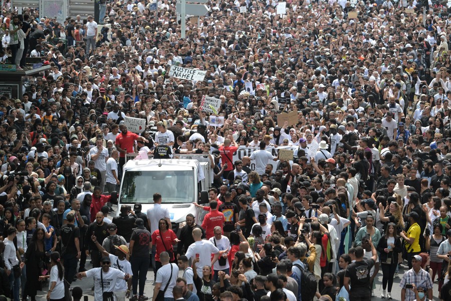 A large number of people in a city street march in protest and gather to watch the march.