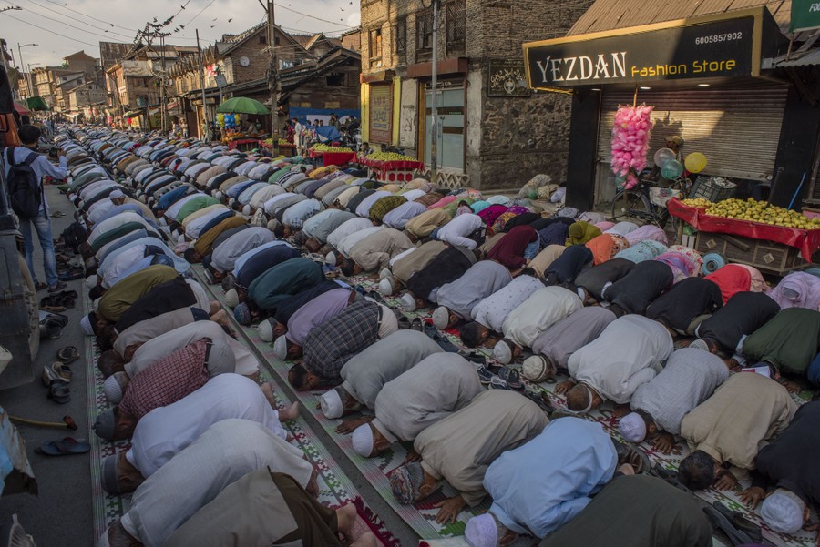 Hundreds of people kneel in prayer, forming several rows filling a street.