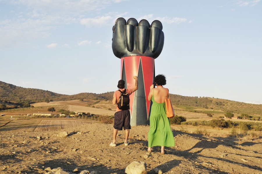 Two people take photographs of a large sculpture shaped like a robotic fist.