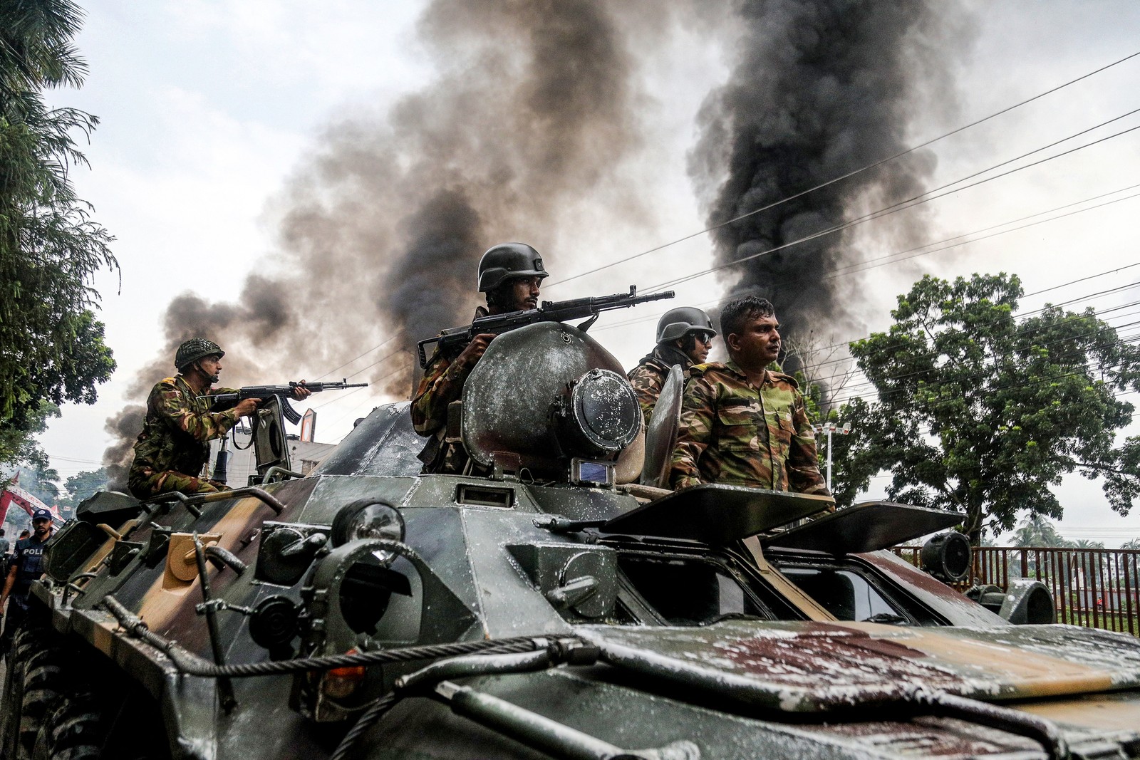 Several soldiers ride in and on an armored vehicle, with black smoke in the background.