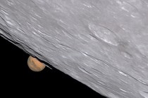 A close view (through a powerful telescope) of the edge of the moon, with the planet Mars half visible behind it.