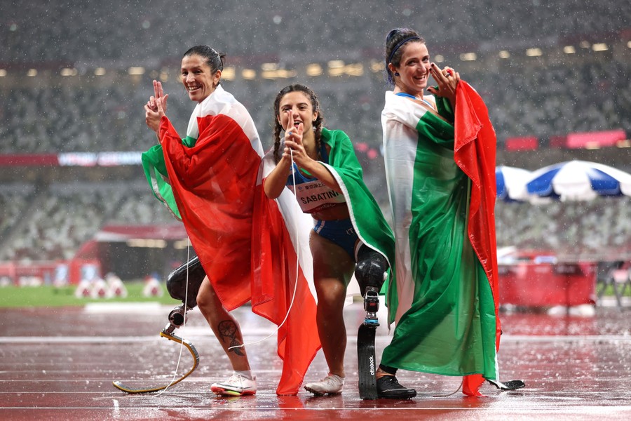 Three paralympic athletes pose on a track in a rainstorm.