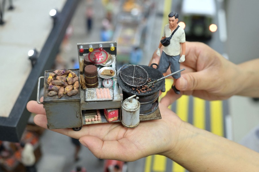 A model maker holds up a model of a person and a street food cart.