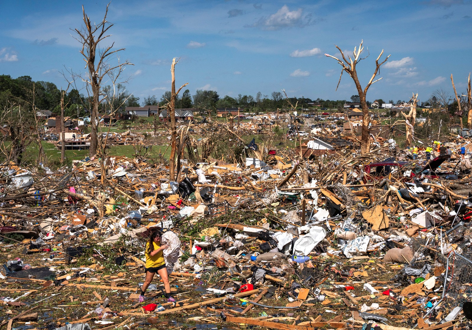 A woman carries her wedding dress after finding it in a vast field of debris left by a tornado.