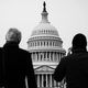 Black and white photograph of two men looking up at the US Capitol building, one holding a phone to his ear