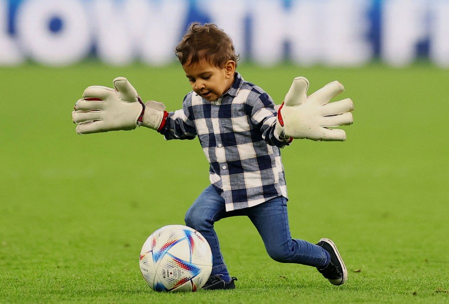 A boy wears huge gloves while playing with a soccer ball on a field.