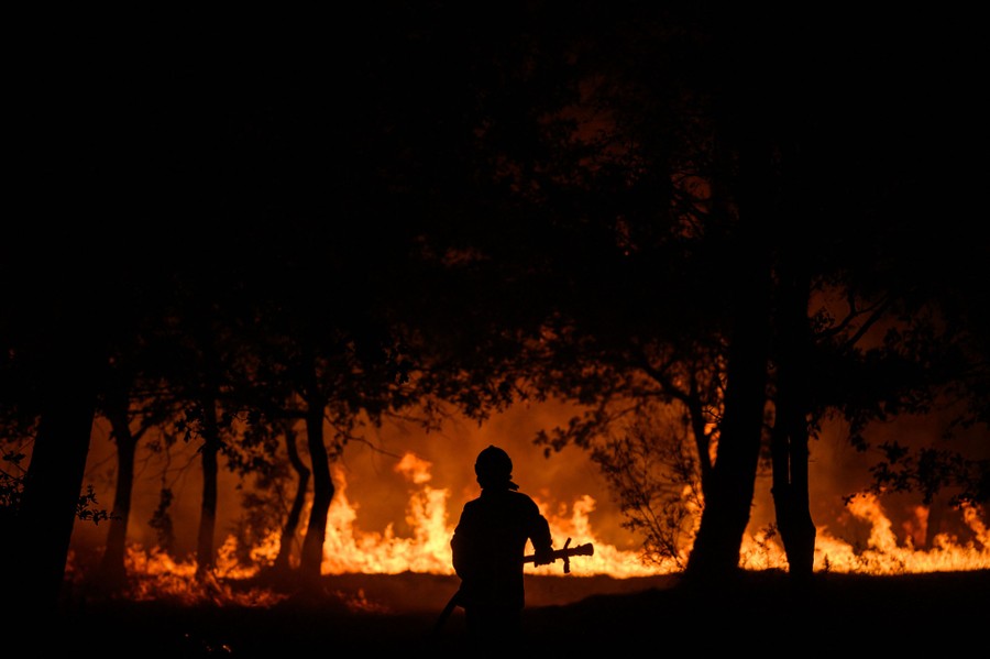 A firefighter stands in front of flames at night, during a wildfire.