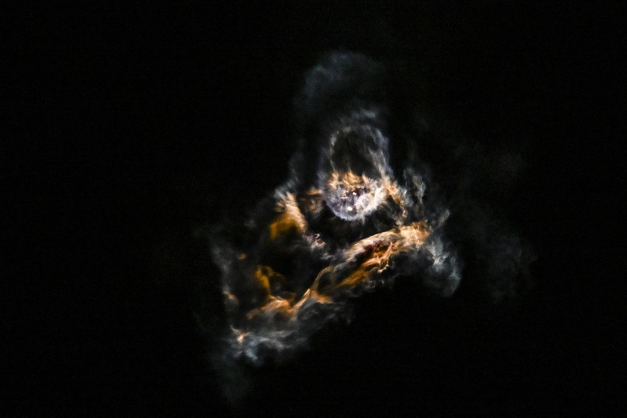 Clouds of exhaust are lit up in the night sky, looking like glowing clouds, or a nebula in space.