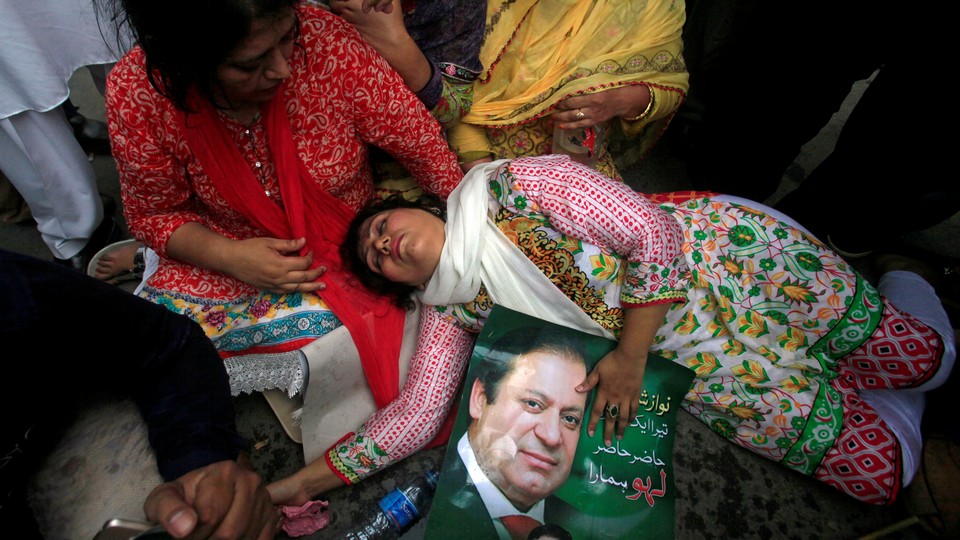 A supporter of Pakistan's Prime Minister Nawaz Sharif passes out on the ground, holding a photo of him.