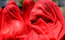Demonstrators stand together, wearing bright-red fabric draped over their heads.