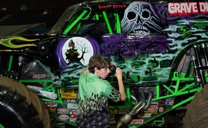 A young man stands beside a monster truck that features a skull on its side.