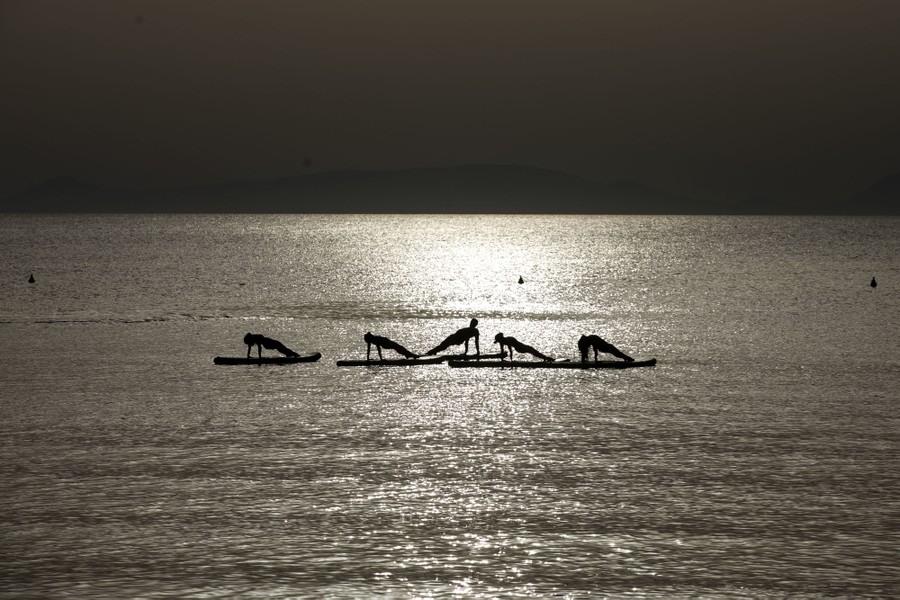 Five people exercise atop floating surfboards.