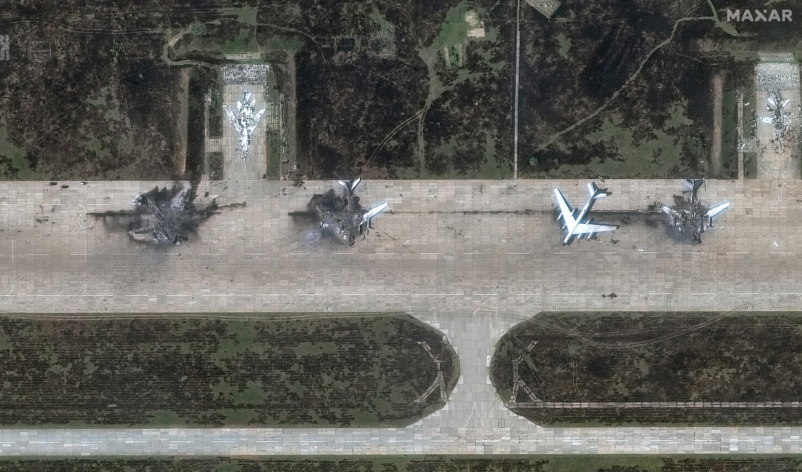 A satellite view of the charred remains of several large bomber aircraft, on an airfield